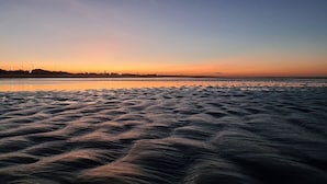 A beach with rippled sand patterns and a distant city skyline at sunset. - POUSADA SONHO DE MAR (Luis Correia)