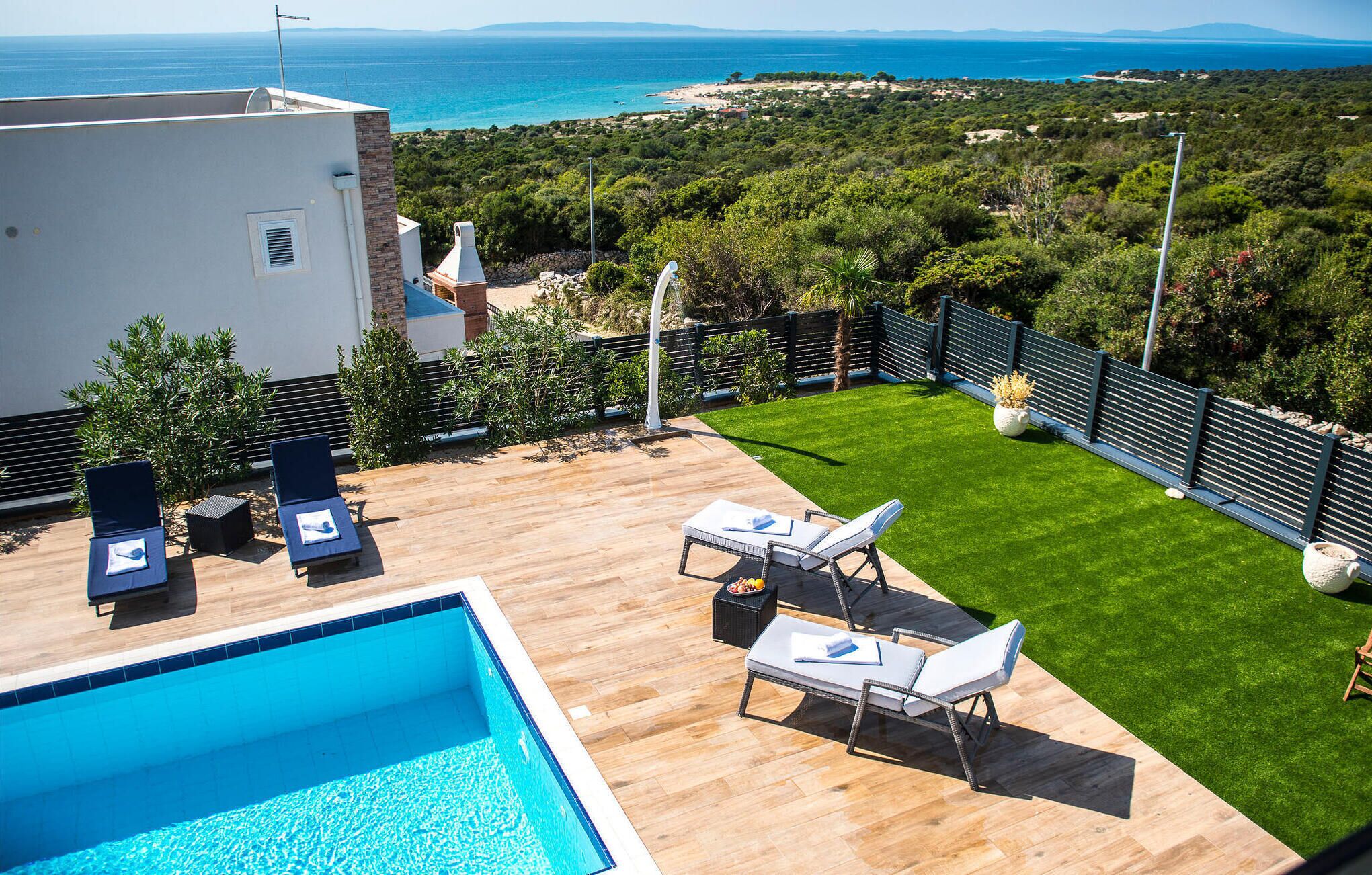 A poolside area with lounge chairs, a small pool, and a view of the sea and greenery.