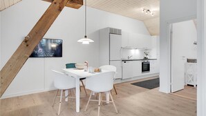A modern kitchen with white cabinetry, a dining area with a white table and chairs, and a wooden ceiling beam. - Amazing home in Grindsted with sauna (Grindsted)