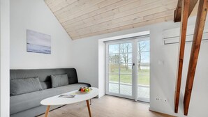 A modern living room with a grey sofa, a white coffee table with fruits, and a large glass door leading outside. - Amazing home in Grindsted with sauna (Grindsted)