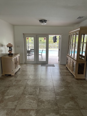 A spacious room with a tiled floor, a large cabinet, and a view of a swimming pool through glass doors.