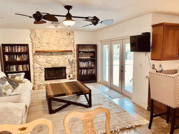 A living room with a stone fireplace, ceiling fans, bookshelves, a sofa, and a television.