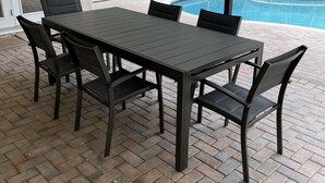 Une terrasse couverte avec une table et des chaises, une piscine et une vue sur les palmiers.