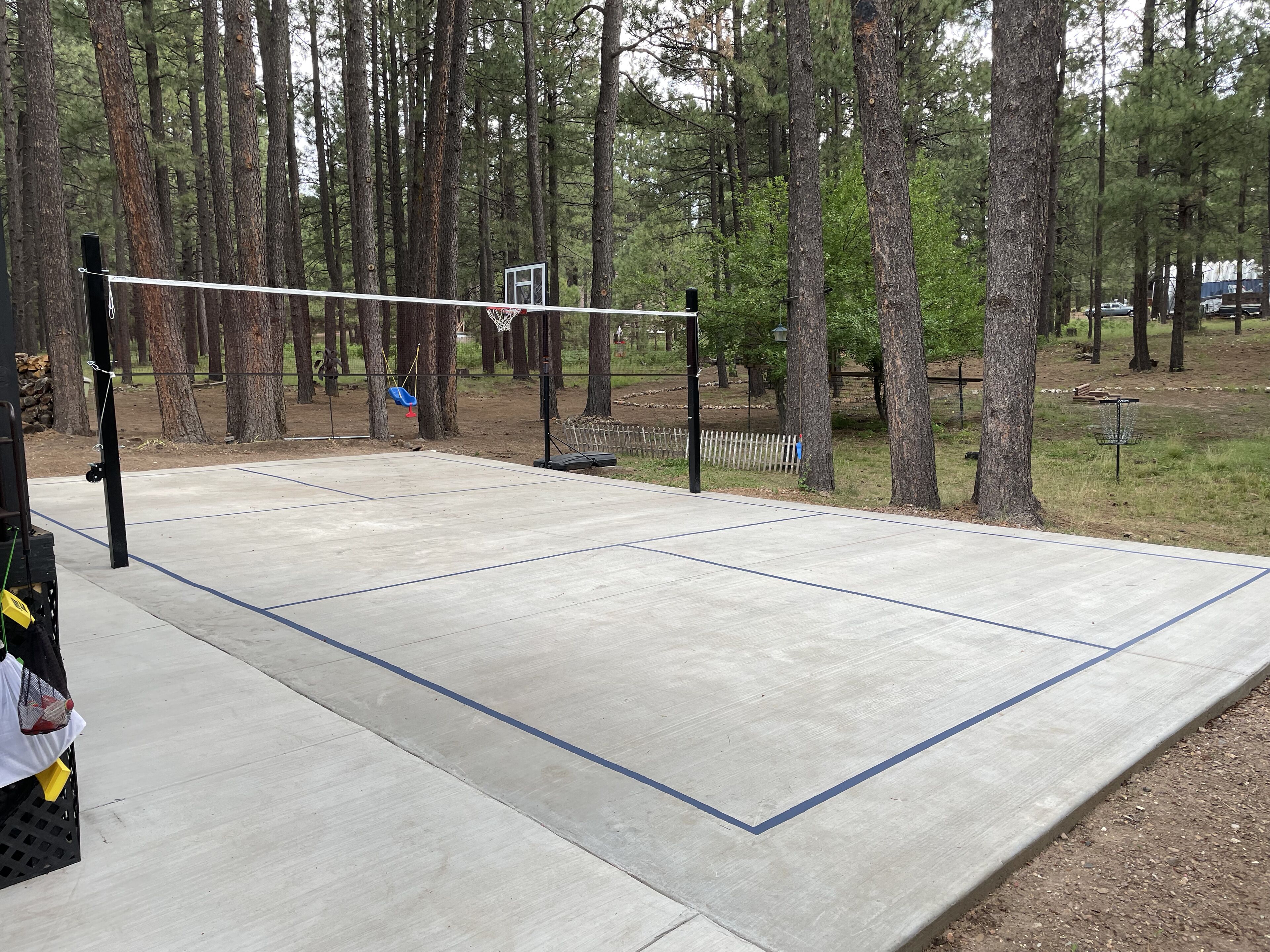 An outdoor basketball court with a net, surrounded by trees.