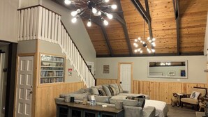 A spacious living room with a large sectional sofa, a wooden staircase, and a ceiling with exposed beams and hanging lights. - Cabin Retreat in Forest Lakes ... 2 hours from the Valley (Forest Lakes Estates)