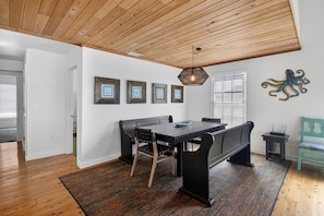 A dining area with a wooden ceiling, a black table with chairs, and framed artwork on the wall.