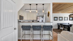 A kitchen with white cabinets, a central island with bar stools, a dining area with a table and chairs, and a ceiling with exposed beams.
