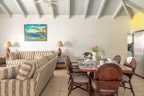A dining area with a table set for four, surrounded by wicker chairs, a sofa, and two lamps. - Oceanfront 3 Bedroom Signature Villa (Tortola)