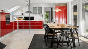 Una cocina moderna con armarios rojos, una zona de comedor con una mesa de madera y sillas negras, y un ventanal que proporciona luz natural.
