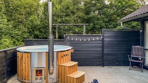 Un jacuzzi con escalones de madera y un tubo de metal, rodeado por una valla de madera y árboles.