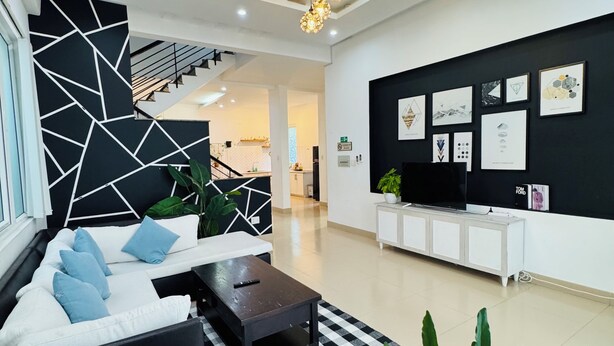 A modern living room with a black and white geometric wall design, a black sofa with blue cushions, a wooden coffee table, and a checkered rug.