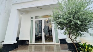 A multi-story building with a central entrance, a balcony on the upper floor, and a small tree in the foreground.