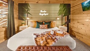 A cozy wooden room with a bed, a nightstand, a lamp, and a wall-mounted TV.