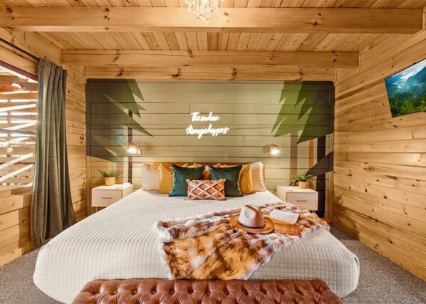 A cozy wooden room with a bed, a nightstand, a lamp, and a wall-mounted TV.