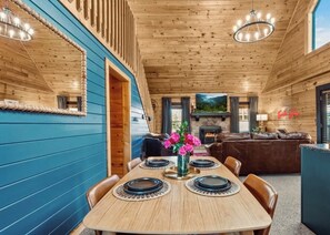A cozy cabin interior with a dining area, a fireplace, and a living room with a sofa and a TV.