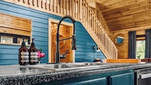 A kitchen with a wooden staircase, a sink, and two bottles of dish soap.