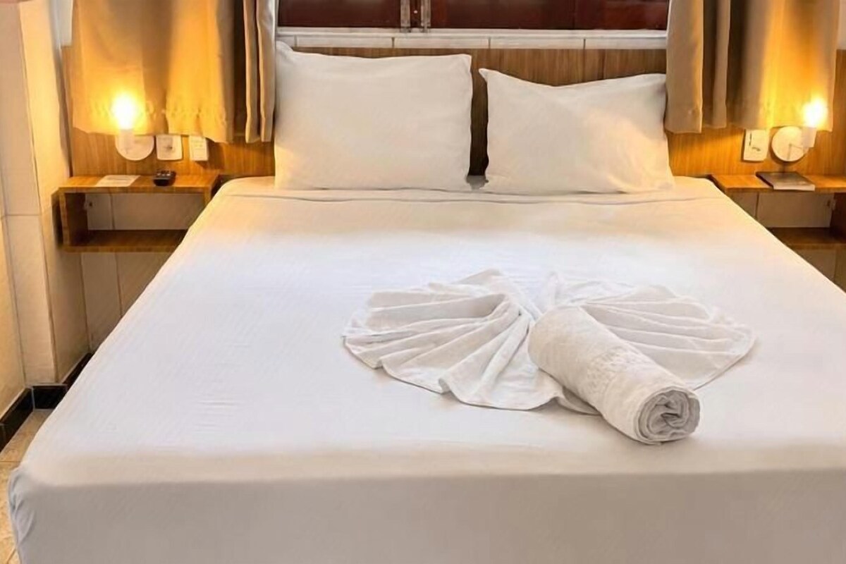 A hotel room with a neatly made bed, two bedside tables with lamps, and a headboard.