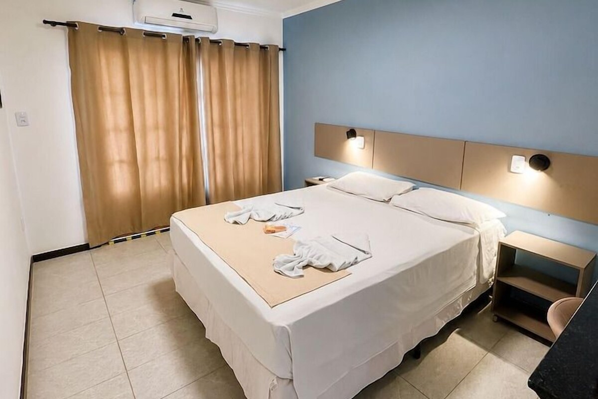 A hotel room with a bed, bedside tables, a desk, and a window with curtains.