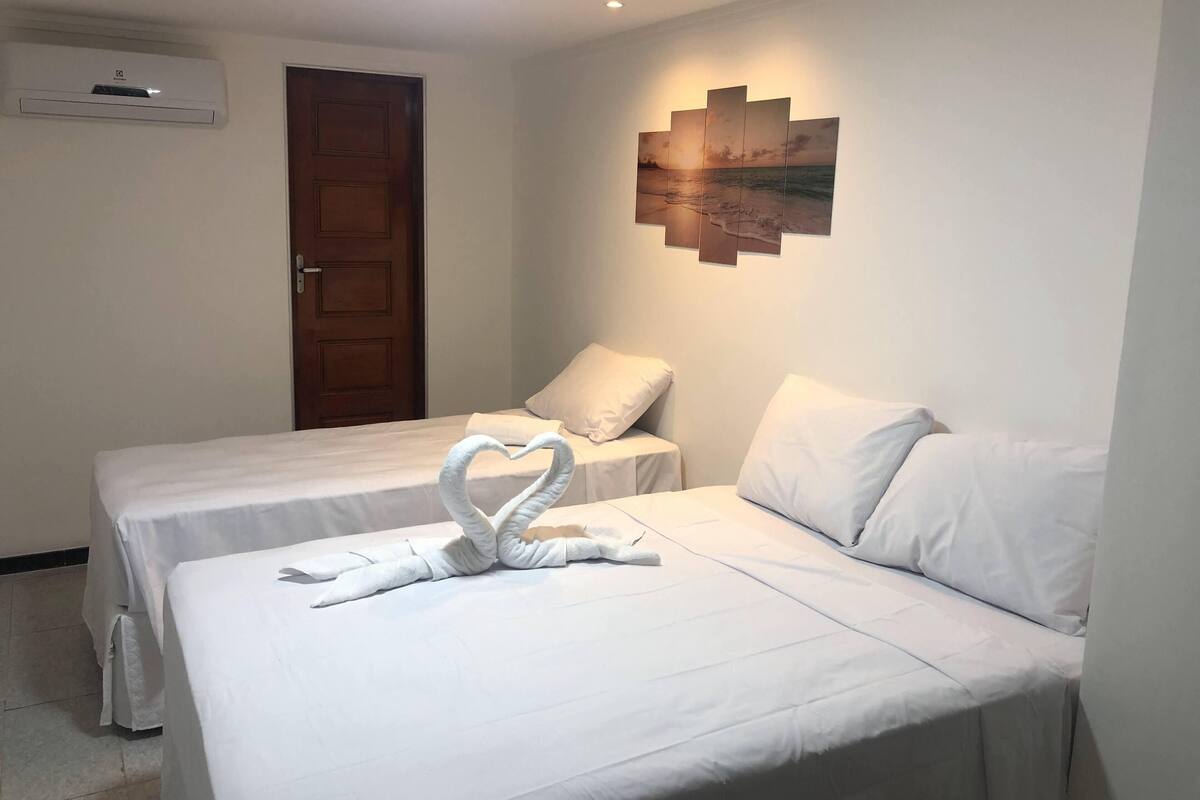 Habitación de hotel con dos camas, una puerta de madera, un equipo de aire acondicionado y una obra de arte colgada en la pared.