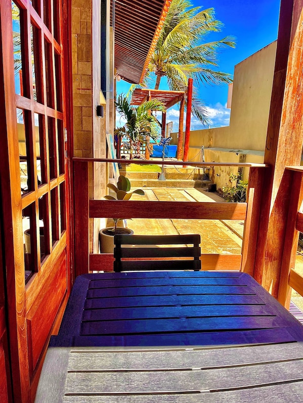An outdoor seating area with a wooden bench and a view of a palm tree and building. - Pousada La Riviera (Maragogi)