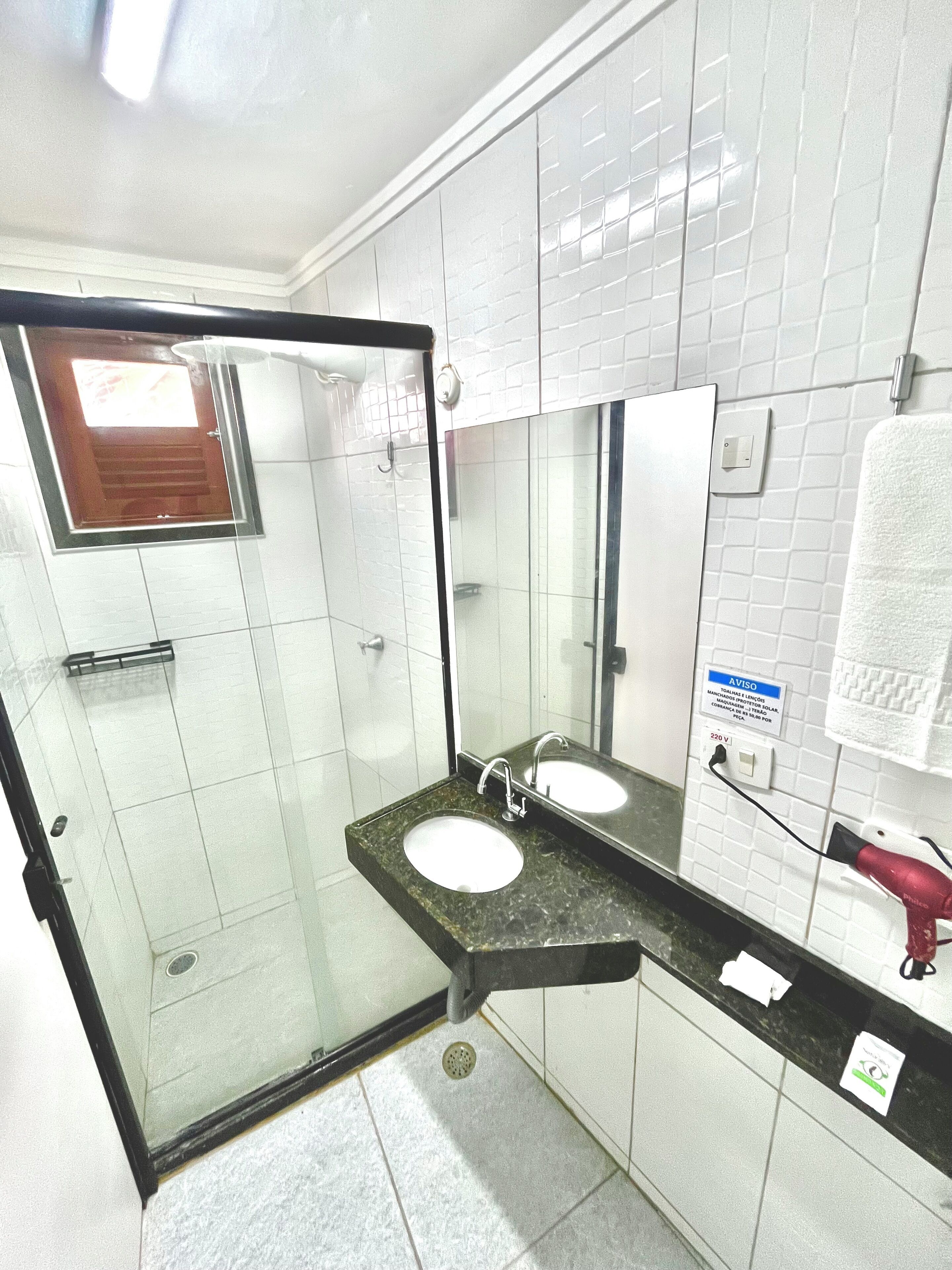 A bathroom with a glass shower enclosure, a sink with a mirror, and a towel hanging on the wall.