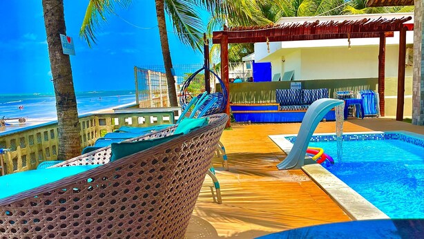 A pool area with a slide, lounge chairs, and a view of the beach. - Pousada La Riviera (Maragogi)