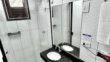 A bathroom with a glass shower enclosure, two sinks with mirrors, and a towel hanging on a rack.