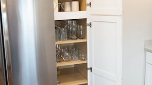 A kitchen with a stainless steel refrigerator, open white cabinets with shelves containing glassware and a kettle. - Spacious and Bright Downtown APT with River View (Ellsworth)