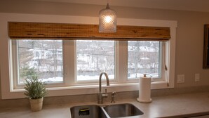 A kitchen with a double sink, a hanging light fixture, and a window with a view of a snowy landscape. - Spacious and Bright Downtown APT with River View (Ellsworth)