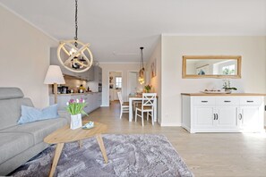 Un salon moderne avec un canapé gris, une table basse en bois et un coin repas comprenant une table et des chaises blanches.