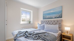 Une chambre à coucher avec un lit, une fenêtre donnant sur un beau paysage, un tableau accroché au mur et une table de chevet avec une lampe.