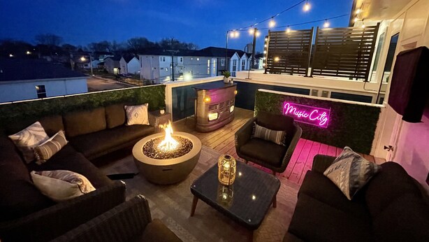 An outdoor patio with a fire pit, seating area, and string lights. - Rooftop Bar ★ Downtown ★ Brand New (Nashville)