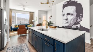 A modern kitchen with a large island, a dining area with a blue sofa, and a living room with a large wall mural. - Rooftop Bar ★ Downtown ★ Brand New (Nashville)
