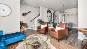 A modern living room with a blue sofa, leather armchairs, a glass coffee table, and a staircase leading to a kitchen. - Rooftop Bar ★ Downtown ★ Brand New (Nashville)
