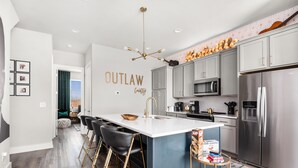 A modern kitchen with a central island, bar stools, stainless steel appliances, and a decorative sign. - Rooftop Bar ★ Downtown ★ Brand New (Nashville)