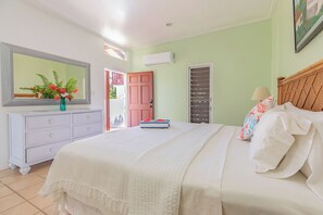 Une chambre à coucher comprenant un lit, une commode, un miroir et une porte donnant sur un espace extérieur.