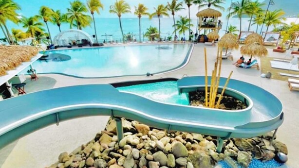 A pool area with a water slide, lounge chairs, and palm trees. - 3-person studio deck 15m2 facing Le Diamant (Le Diamant)