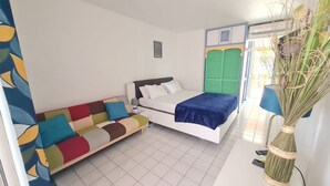 A bedroom with a bed, a colorful sofa, a green door, and a plant. - 3-person studio deck 15m2 facing Le Diamant (Le Diamant)