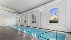 Ein überdachter Schwimmbereich mit großen, bogenförmigen Fenstern, Glaswänden und einem gefliesten Boden.