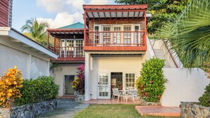 A two-story house with a balcony, a patio with chairs, and a stone wall. - Oceanfront 2 Bedroom Premium Villa (Tortola)