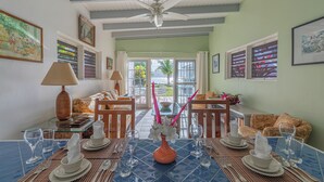 A dining area with a table set for four, a ceiling fan, and a view through a glass door to the outside. - Oceanfront 2 Bedroom Premium Villa (Tortola)