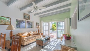 A spacious living room with a high ceiling, a ceiling fan, a sofa, a coffee table, and a dining area with chairs and a table. - Oceanfront 2 Bedroom Premium Villa (Tortola)