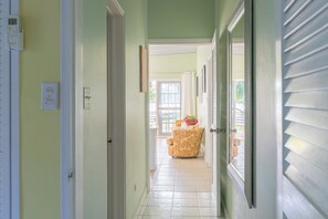 A hallway with a door leading to a room with a view, a chair, and a plant.