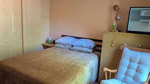 Un dormitorio con cama, una mecedora, una mesita de noche y un ventilador de techo.