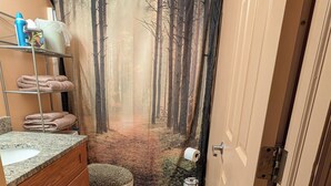 Baño con inodoro, lavamanos y cortina de ducha con motivo de un bosque.