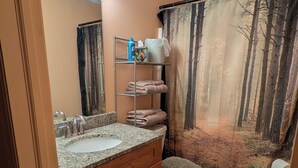Un baño con tocador, lavabo, espejo y cortina de ducha con paisaje de bosque.