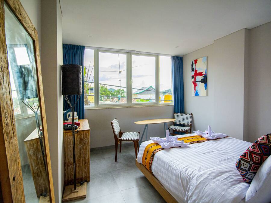 Habitación de hotel con cama, una mesita, una silla y ventana con cortinas.