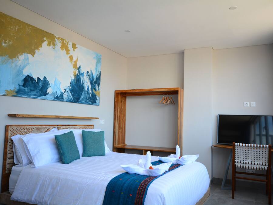 A hotel room with a large bed, a wooden headboard, a TV, and a painting on the wall.