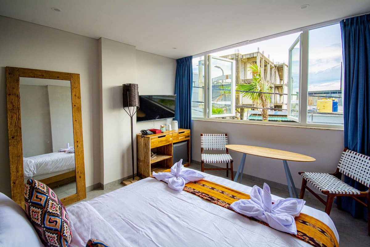 A hotel room with a bed, a desk, a TV, a chair, and a window with a view of a building.