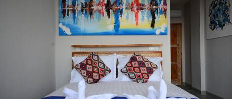 A hotel room with a large bed, two patterned pillows, a blue-striped bedspread, and a painting above the bed.